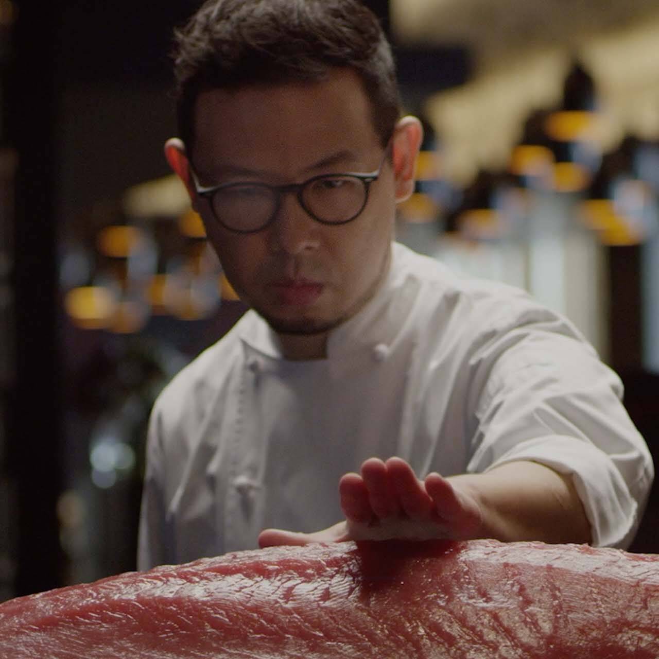 A chef demonstrating precision whilst sizing up a piece of Tuna