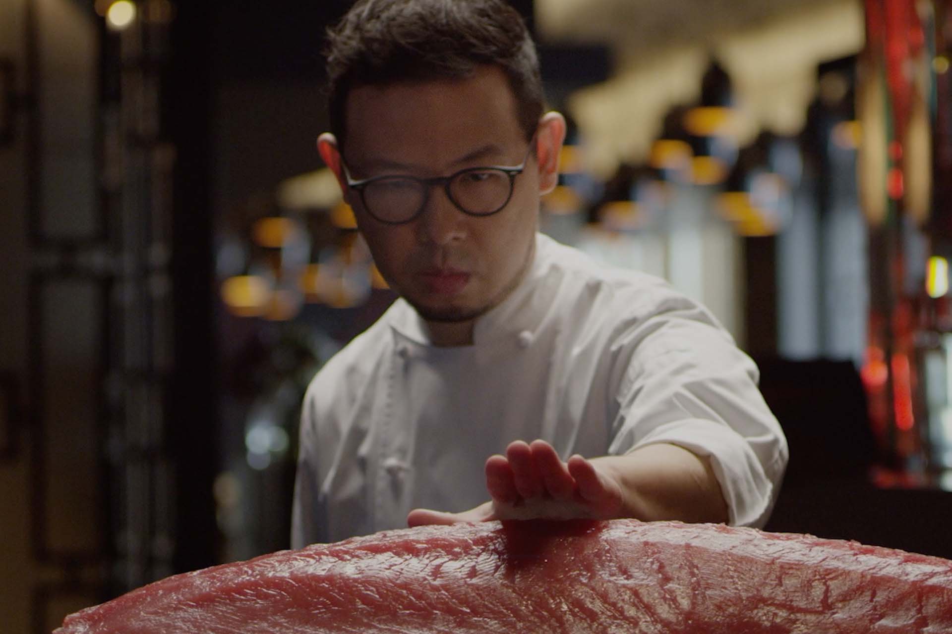 A chef demonstrating precision whilst sizing up a piece of Tuna