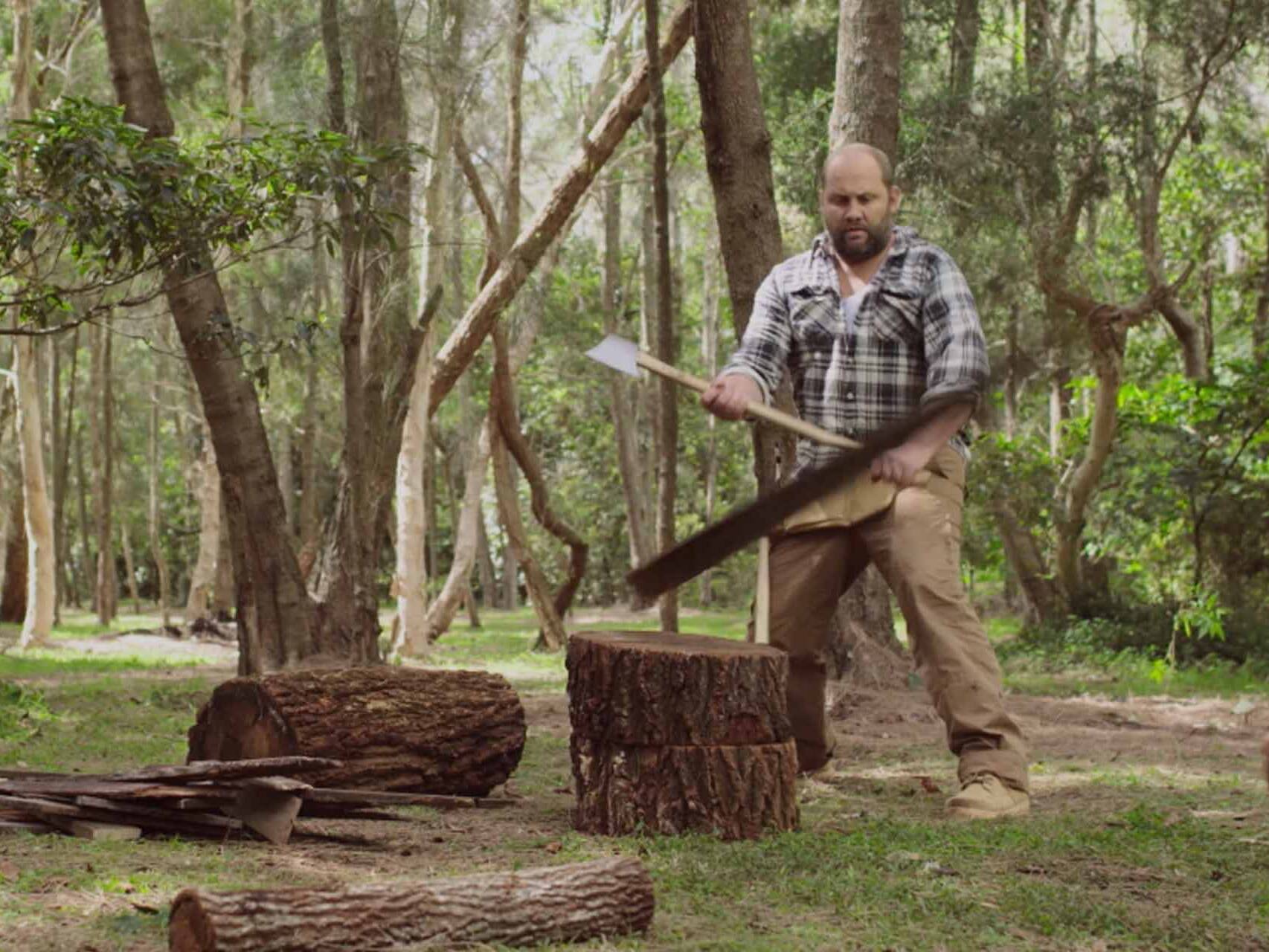 Man comically chopping wood in green riverside setting.