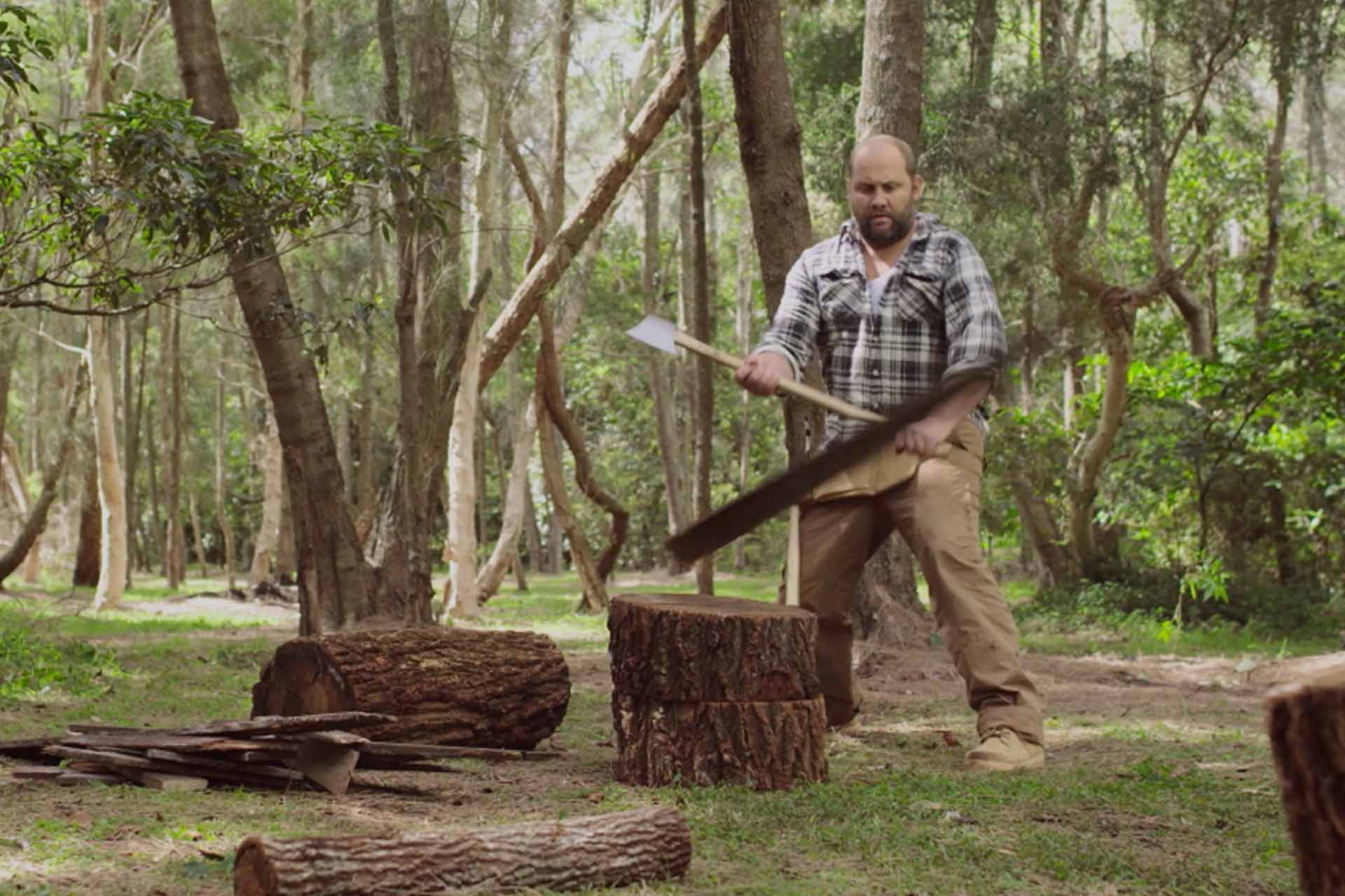 Man comically chopping wood in green riverside setting.