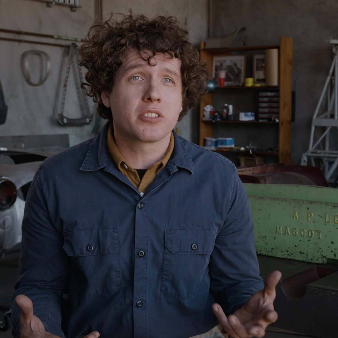 Man sat talking to camera in interesting car workshop