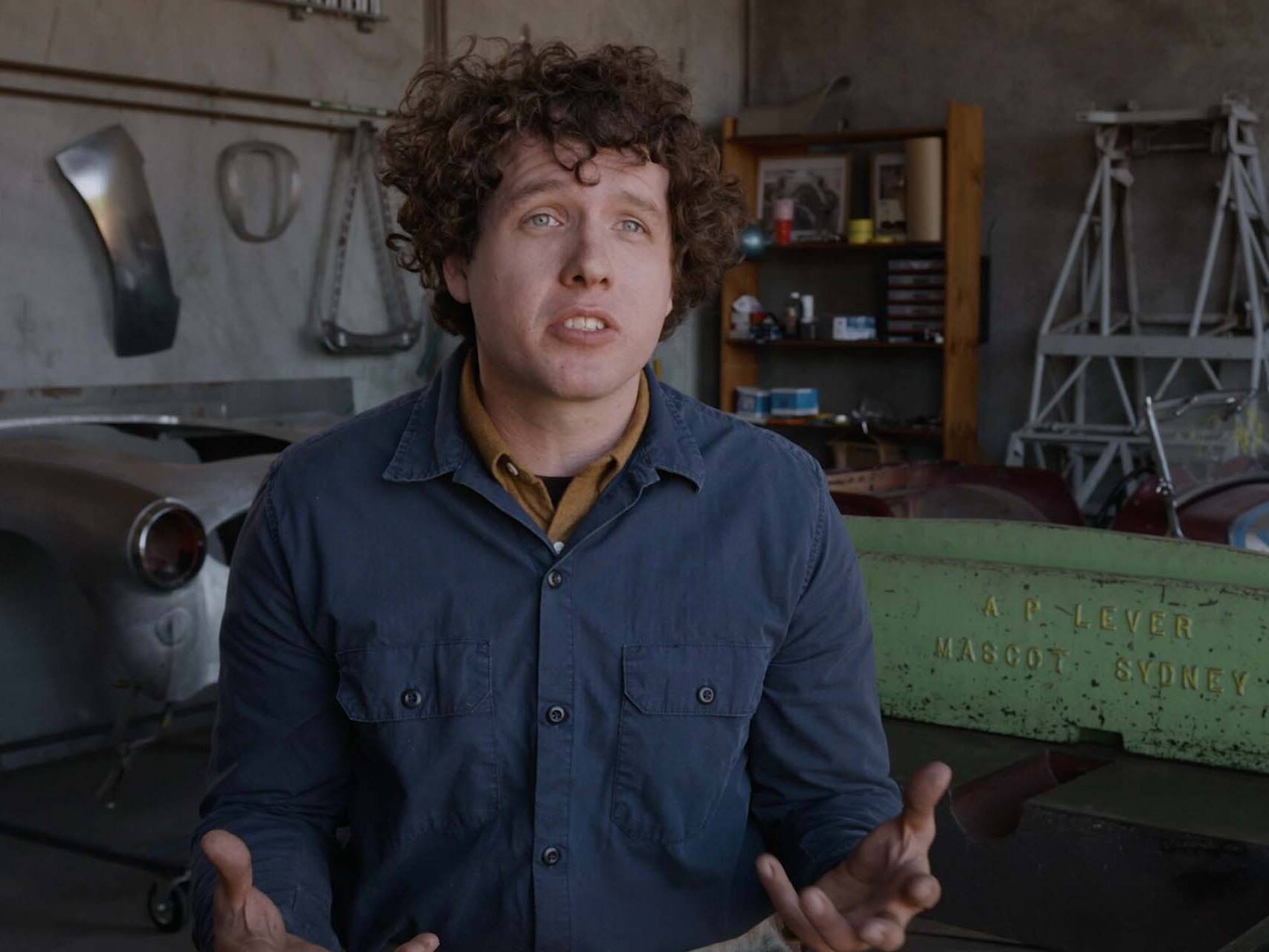 Man sat talking to camera in interesting car workshop