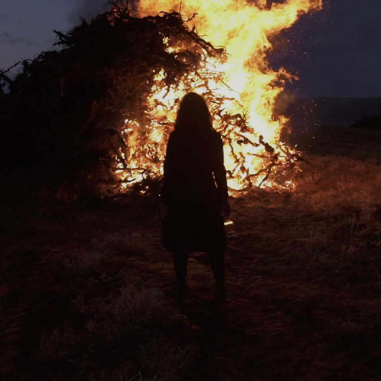Women stood in front of huge pile of burning vines at night