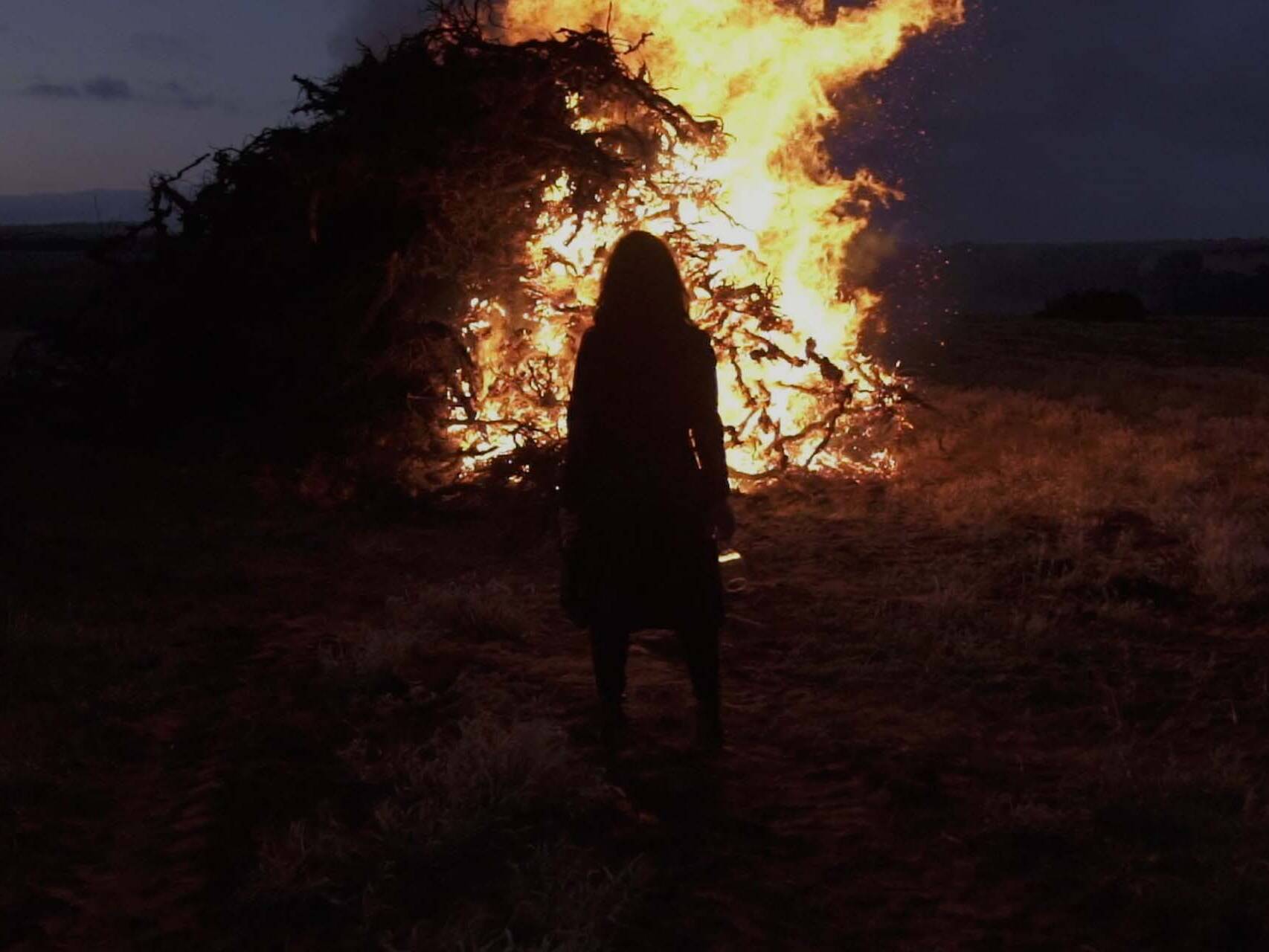 Women stood in front of huge pile of burning vines at night