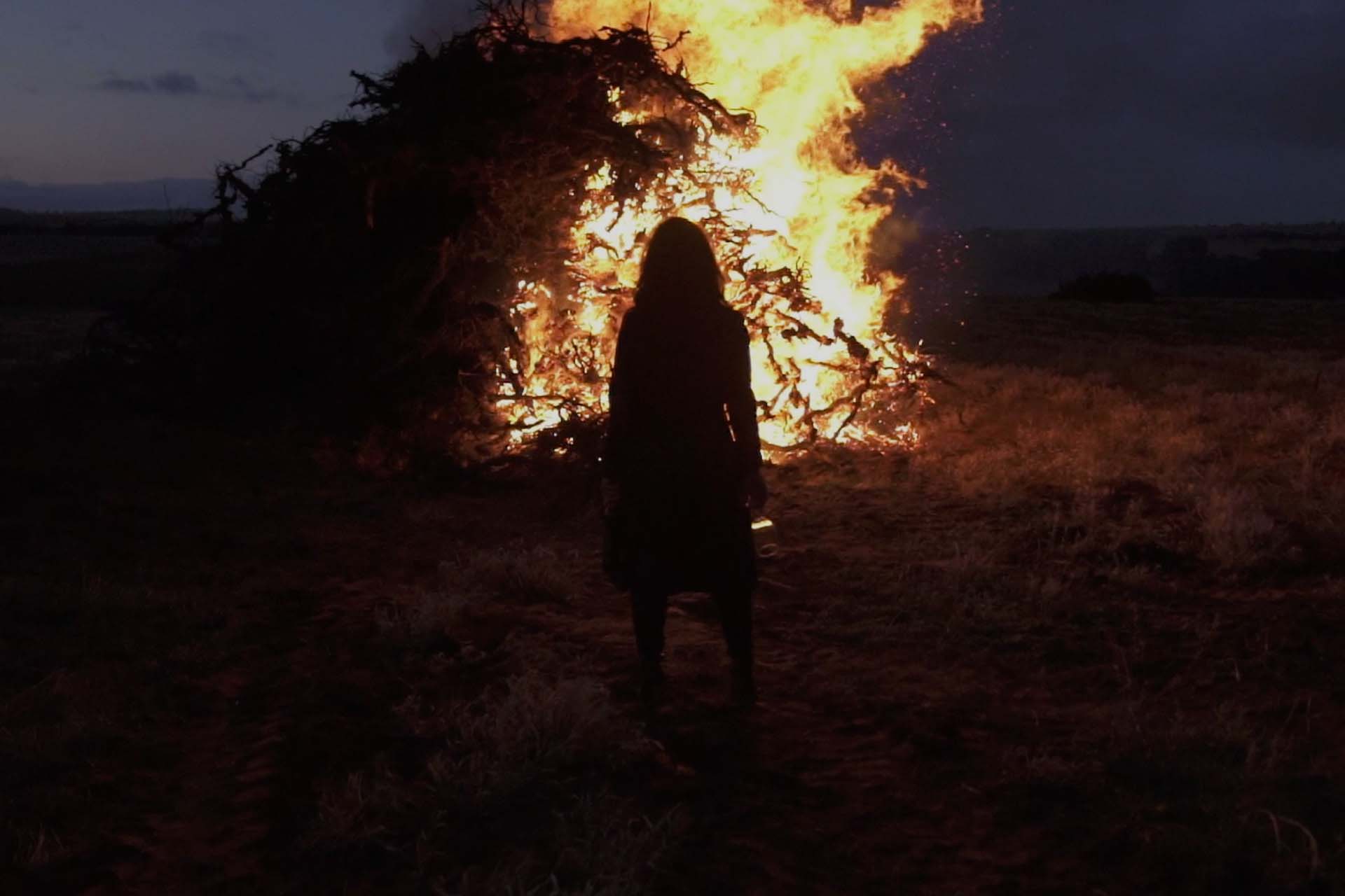 Women stood in front of huge pile of burning vines at night